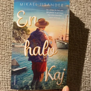 En halv Kaj - En färgstark bok med sommarkänsla! Omslaget visar en person i semesterkläder vid havet, med båtar och solnedgång. Perfekt för dig som gillar berättelser om äventyr, relationer och nya platser.