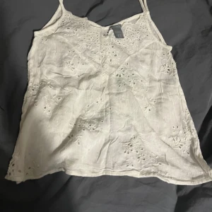 Vit broderad linnetopp från Lindex XS - Supersöt vit linnetopp från Lindex i storlek XS. Toppen har tunna axelband och är dekorerad med broderade blommor och hålmönster för en romantisk vibe. Perfekt till sommaren och lätt att matcha med jeans eller kjol.