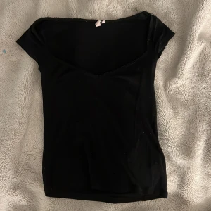 Romance top från Nelly  - En svart, tight topp från Nelly med v-ringning och korta ärmar. Romance top med korta ärmar 