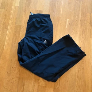 Svarta träningsbyxor från Adidas - Svarta träningsbyxor från Adidas. Byxorna har resår i midjan, raka ben och dragkedjor vid bensluten. Perfekta för träning eller chill