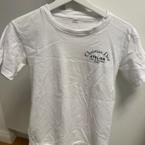 Vit t-shirt - Vit t-shirt med svart tryck fram och bak. Klassisk rund hals och korta ärmar. Tillverkad i 100% bomull för en skön och avslappnad känsla. Perfekt för dig som gillar stilrena och exklusiva plagg med tydlig logga.