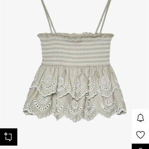  broderad topp med volang - Supersöt topp med smala axelband och broderade detaljer i vitt. Toppen har smockad överdel och dubbla volanger med snyggt broderade kanter och hålmönster. 