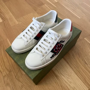 Gucci ace snake - Ett par snygga gucci ace snakes i mint condition. Skorna har vit snörning, rund tå och platt sula. Baksidan har röda och gröna detaljer. Perfekta för dig som vill sticka ut med lyxig streetstyle. Smått använda men som nya, inga skador varken utanför eller innanför skorna.