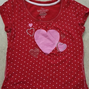 T-shirt - Supersöt röd t-shirt med vita prickar och flera rosa hjärtan framtill. Rund halsringning med vit kant och korta ärmar. Perfekt för dig som gillar gulliga detaljer och färgglada plagg.