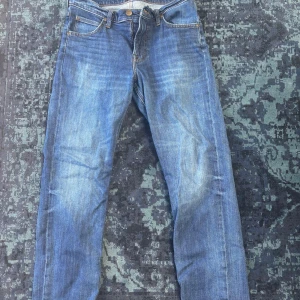 Blå jeans från Lee W29 L30 - Säljer ett par klassiska blå jeans från Lee i modellen WEST. Jeansen har raka ben, fem fickor och snygga slitningar framtill. De är tillverkade i bomull och har Lee-logga på bakfickan. Perfekta för en avslappnad och stilren look.