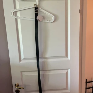 Svart smalt bälte med gulddetaljer 80cm - Snyggt svart bälte med smal design och guldfärgat spänne. Perfekt för att ge en stilren touch till jeans eller kjol. Bältet har flera hål för justerbar passform och enkla gulddetaljer vid spännet.