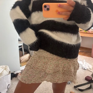 Blommig volangkjol med smock - Supersöt kort kjol med blommigt mönster i rosa och grönt på beige botten. Kjolen har smock i midjan och volangdetaljer som ger en flowy och feminin vibe. Perfekt för varma dagar och lätt att styla med en enkel topp eller stickad tröja.