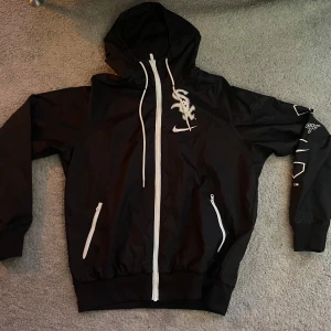 Svart Nike White Sox vindjacka S Man - Svart vindjacka från Nike x Chicago White Sox med vit dragkedja, huva och tryck på bröstet och ärmen. Jackan har två fickor med dragkedja. Köptes förra året och har används fåtal gånger. Pris kam diskuteras i snabb affär:)