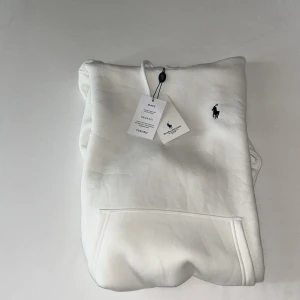 Vit hoodie från Polo Ralph Lauren - Säljer en stilren vit hoodie från Polo Ralph Lauren i storlek S. Tröjan har huva med snörning, klassisk känguruficka och den  loggan på bröstet. Tillverkad i mjuk bomull för en skön och avslappnad look.