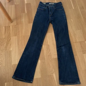 Levi's 725 High Rise Bootcut Jeans - Säljer ett par mörkblå Levi's 725 High Rise Bootcut jeans i klassisk denim. De har hög midja, bootcut-ben och snygga kontrastsömmar. Perfekta om du gillar en tidlös look med lite 70-talsvibe. Ikonisk läderpatch bak och femficksmodell.