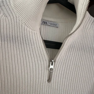 Vit stickad tröja med dragkedja från Zara - Säljer en vit stickad tröja från Zara med hög krage och dragkedja framtill. Tröjan har lång ärm och är ribbstickad vilket ger en snygg struktur. Perfekt för lager-på-lager och stilrena outfits. Storlek M