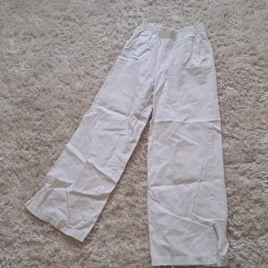 Vita vida byxor med resårmidja - Säljer ett par vita byxor med resår i midjan och raka, vida ben. Byxorna har en avslappnad passform och är tillverkade i ett lätt tyg, perfekta för varmare dagar.