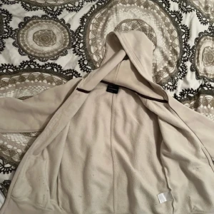 Beige hoodie från Peak Performance - Säljer en beige hoodie från Peak Performance med dragkedja och huva. Tröjan har tryckt logga på bröstet och är tillverkad i mjukt material. Perfekt för en avslappnad stil.