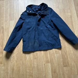 Marinblå vindjacka från Polo Ralph Lauren - Säljer en marinblå vindjacka från Polo Ralph Lauren med huva och dragkedja framtill. Jackan har klassisk design med diskret logga på bröstet och praktiska fickor. Perfekt för blåsiga dagar och enkel att matcha med olika outfits.