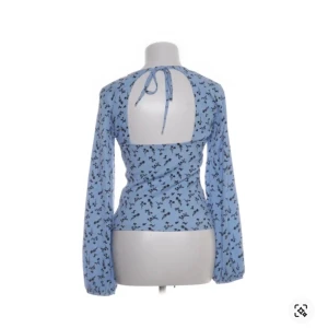Blommig blå blus med öppen rygg och knyt - Säljer en ljusblå blus med svart blommigt mönster. Toppen har långärmade puffärmar, v-ringning och en snygg öppen rygg med knytband i nacken. Perfekt för dig som vill ha något unikt och trendigt! Toppen är från Gina i storlek M men kan även passa S och L. Köpte toppen ny men lånar bilder av Sellpy! Skriv vid frågor, pris är diskuterbart 🤍