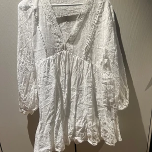Vit  klänning med volang och spetsdetaljer - Säljer en vit klänning med v-ringning, spetsdetaljer och volang nedtill.