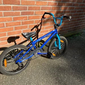 Blå BMX-cykel med svart sadel - Säljer en blå BMX-cykel med svart sadel. Köpte cykeln för 5000kr och har inte använt den så mycket. Den är lite rostig på handtaget men går att få bort, däcken är hårda och pumpade. Cykeln har två stycken pinnar vid sidan som går att stå på och göra trix med. 