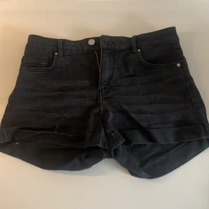 Svarta jeansshorts från H&M - Svarta jeansshorts från H&M i klassisk femficksmodell med uppvikta benslut. Shortsen har normal passform och stängs med dragkedja och knapp. Materialet är en blandning av bomull, polyester och elastan för lite stretch. Säljer för att de var för små och jag kunde ej returnera.