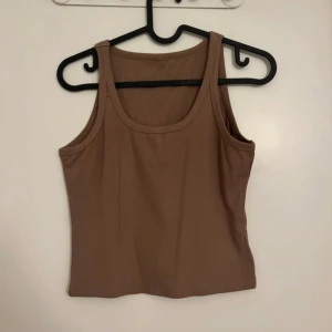 Brun ribbad linnetopp - Säljer en enkel och stilren brun ribbad linnetopp med breda axelband och rundad halsringning. Perfekt att matcha med jeans eller kjol för en avslappnad look.