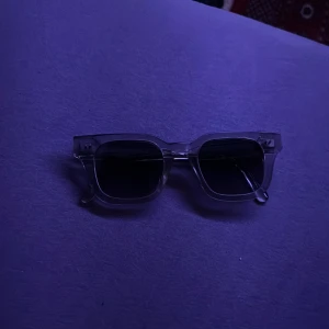 Solglasögon från CHIMI - Snygga solglasögon från CHIMI med transparent båge och mörka fyrkantiga glas. Perfekt accessoar för att lyfta din stil med en modern och stilren look. Passar dig som gillar trendiga och klassiska former.