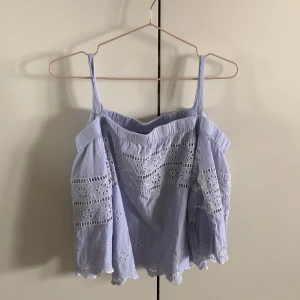 ljusblå med vit Brodyr broderie anglaise linneblus - Säljer en ljusblå linneblus offshouldermed tunna axelband och vackra broderade spetsdetaljer. Toppen har en luftig passform och dekorativa hålbroderier längs hela plagget. Perfekt för varma dagar!