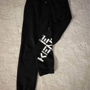 Svarta mjukisbyxor från KENZO - Svarta mjukisbyxor med resår i midjan och vid bensluten. Ena benet har en stor vit textdetalj som ger en sportig look. Perfekta för en avslappnad stil eller till träning.