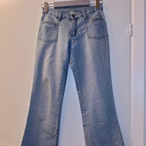 Ljusblå bootcut jeans - Säljer ett par ljusblå jeans med bootcut passform och låg midja. Jeansen har två stora framfickor och klassisk knappgylf. Perfekta för dig som gillar en retroinspirerad look. Inga fickor där bak som får jeansen att sticka ut från det ordinala! 