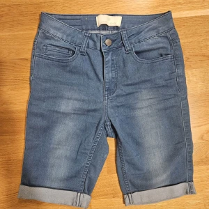 Blå jeansshorts från Pieces - Snygga blå jeansshorts från Pieces med klassisk femficksdesign och uppvikta benslut. Shortsen har normal passform och stängs med knapp och dragkedja. Perfekta för varma dagar och enkla att matcha med olika toppar.