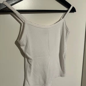 Vit ribbad linnetopp - Säljer en enkel och stilren vit ribbad linnetopp med smala axelband. Perfekt att matcha med jeans eller kjol för en avslappnad look. (aldrig använd) 