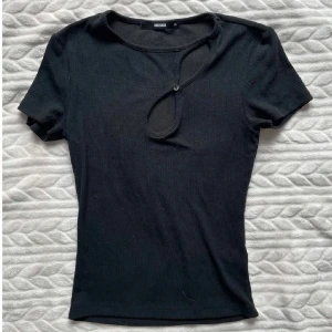 Svart topp m cool design  - Säljer en svart topp från BikBok i storlek XS. Toppen har korta ärmar och en unik öppning och knappdetalj vid halsringningen som skapar en snygg design. Perfekt till många olika outfits! 💞