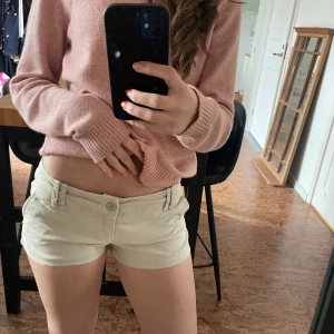 Beiga låga shorts med fickor - Säljer ett par beiga shorts med låg midja och klassiska fickor fram och bak. Shortsen har bälteshällor och stängs med dragkedja och knapp. Perfekta för varma dagar och enkel att matcha med olika toppar.