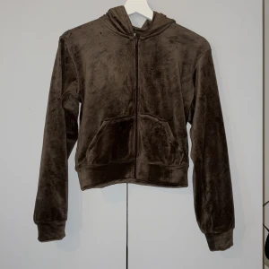 Brun tröja med huva - Mysig brun fleecejacka med huva och dragkedja framtill. Jackan har två fickor på magen och långa ärmar med muddar. Perfekt för kyliga dagar när du vill vara både bekväm och snygg.
