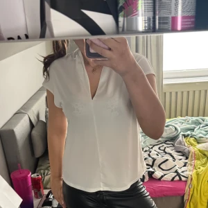 Vit blus med v-ringning - Säljer en stilren vit blus med v-ringning och korta ärmar. Perfekt till både jeans och kjol för en enkel men snygg look. Blusen har en rak passform och är tillverkad i ett lätt material.