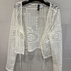 Vit virkad kofta från H&M - Säljer en vit virkad kofta från H&M med långa ärmar och knyt framtill. Koftan har ett genombrutet spetsmönster och är perfekt att slänga över en topp eller klänning.