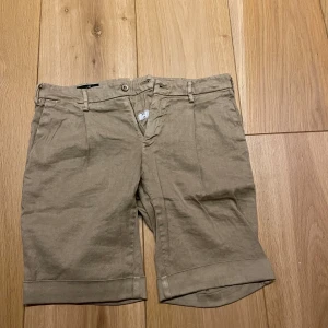 Beiga shorts med uppvikta ben - Snygga beiga shorts med uppvikta ben och klassisk passform. De har bälteshällor, knapp och dragkedja framtill samt två bakfickor med knapp. Perfekta för varma dagar.
