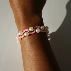 Armband med pärlor och rosa pärlor - Säljer ett sött armband med vita pärlor och små rosa pärlor, ihop med guldfärgad kedja. Armbandet har ett lekfullt och färgglatt utseende, perfekt för att ge din stil en extra touch Eller som en present. Går att få den i andra färger ( blå, grön och vit). 