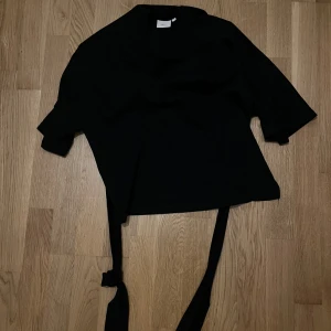 Svart topp med knytband från Nelly - Säljer den virala Nelly toppen då den inte riktigt är min stil. Tröjan är i mycket bra skick och nästan aldrig använd❤️