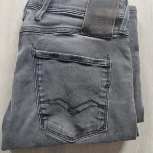 Grå Replay Anbass Hyperflex jeans - Säljer ett par grå Replay Anbass Hyperflex jeans med klassisk femficksdesign och svarta sömmar på bakfickorna. Jeansen har slim passform och är tillverkade i stretchigt material för extra komfort. Perfekta för dig som gillar stilrena och bekväma jeans. På sista bilden ser man ett litet hål som sitter på vänster ben under knät men det är inget man märker. Priset e ej hugget I sten och om du har mer frågor så tveka inte att skriva.