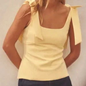 Gul linnetopp med rosettband - Söt gul linnetopp med breda axelband som knyts i rosetter på axlarna. Toppen har en rak halsringning och är figurnära i modellen. Perfekt för varma dagar och ger en fräsch look. Har aldrig använt, prislappen sitter kvar. 