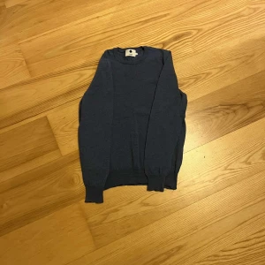 Blå stickad tröja från NN07 - Säljer en stilren blå stickad tröja från NN07 i storlek S. Tröjan har rund halsringning och långa ärmar med ribbade muddar vid ärmslut och nederkant. Perfekt för lager-på-lager och enkel att matcha med jeans eller chinos.