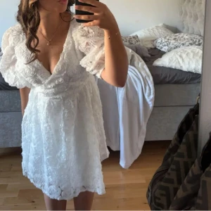 Studentklänning - Säljer min älskade studentklänning från bubbelroom🥰Det är en  vit kortklänning med v-ringning och puffiga trekvartsärmar. Klänningen har spetsditalejer i blommönster. Passar perfekt till både ursprung och mottagning☀️Pris går att diskutera vid snabb affär!!