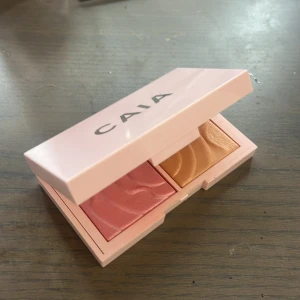 CAIA duo highlighter och rouge - Säljer en CAIA duo med highlighter och rouge i en snygg rosa ask med spegel. Rouget är i en mjuk rosa nyans och highlightern är guldig. Perfekt för att ge ansiktet lyster och färg. Smidig att ha med i väskan.