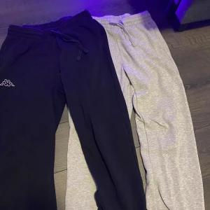 Svarta och grå mjukisbyxor Kappa - Två par mjukisbyxor, en och en grå  från kappa. Båda har är i mjukt material, perfekta för chill dagar eller när du vill vara bekväm. Klassisk passform och elastisk midja så de är väldigt onesize fits many.