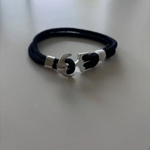 Marinblått armband med silverfärgat ankare - Stilrent marinblått armband med ett coolt silverfärgat ankare som lås. Armbandet har en marin känsla med detaljer i vitt och passar perfekt för dig som gillar enkel men snygg design.