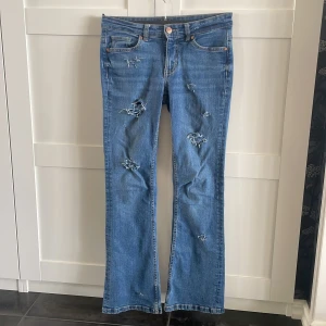 Blå bootcut jeans med slitningar - Snygga blå jeans med bootcut passform och slitna detaljer framtill. Klassisk femficksmodell med knapp och dragkedja. Jeansen har en avslappnad vibe och är perfekta för dig som gillar en lite mer edgy stil. Hålen är gjorda själv.