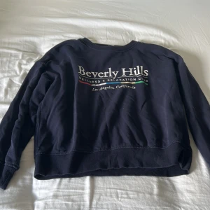 Mörkblå Beverly Hills sweatshirt H&M - Mörkblå sweatshirt från H&M med trycket 'Beverly Hills Wellness & Relaxation Club' framtill. Tröjan har rund hals, långa ärmar och en relaxed fit. Perfekt för en chill och avslappnad stil. Materialet är mjuk bomullsmix som känns skönt mot huden.