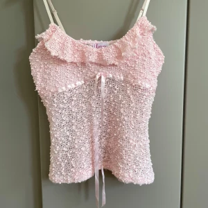 Rosa linnetopp  - Supersöt ljusrosa  linnetopp  med smala axelband, volangkant upptill och dekorativt satinband framtill. Toppen har en bubblig struktur och är lätt transparent, perfekt för en söt och romantisk look. Volang kanten är rå klippt. Några enstaka paljetter. 