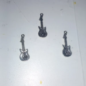 Halsbandshänge elgitarr i silverfärg - Coolt halsbandshänge i form av en elgitarr, perfekt för dig som älskar musik och vill ha en unik detalj. Hänget är i silverfärgad metall med fina detaljer som strängar och knappar. Passar att hänga på en kedja eller använda som charm.