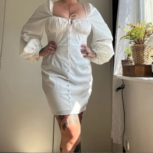 Vit kortklänning från Glamorous - Supersöt vit kortklänning från Glamorous med puffiga långärmar, knappar framtill och snörning vid bysten. 