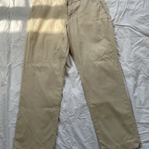 Beiga bomullsbyxor Polo Ralph Lauren - Snygga beiga byxor från Polo Ralph Lauren, modell Preston Pant. Tillverkade i 100% bomull med rak passform och klassisk look. Perfekta för dig som gillar stilrena och bekväma byxor med en tidlös vibe. Svart fläck under höger backficka men inget man tänker på.